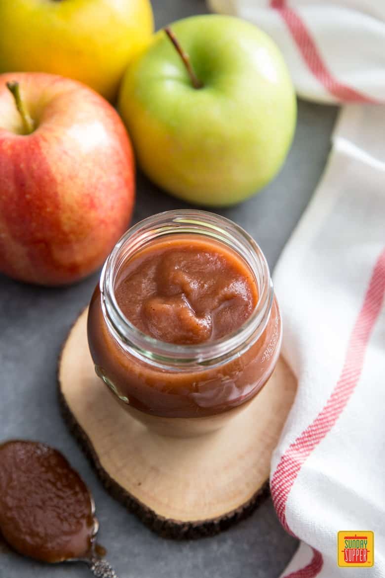 Slow cooker apple sauce in a glass jar next to three varieties of apple