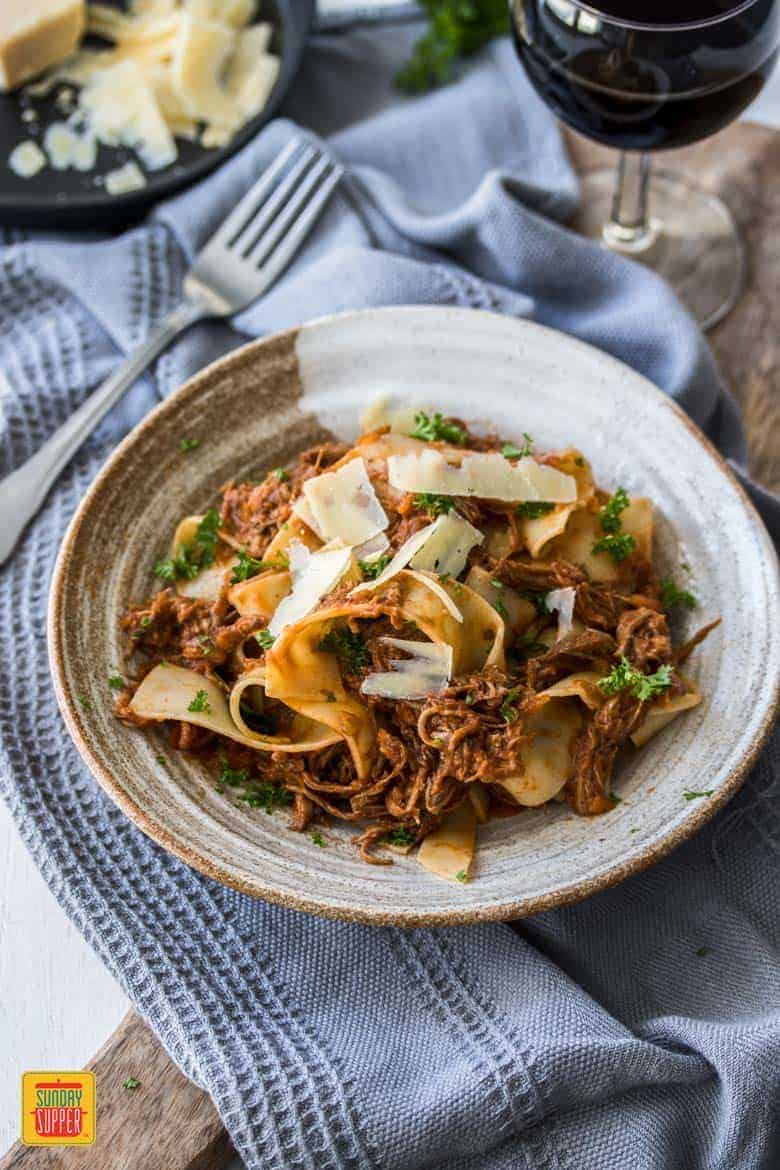 Slow Cooker Beef Ragu served over pappardelle pasta on a plate topped with shaved Parmesan cheese