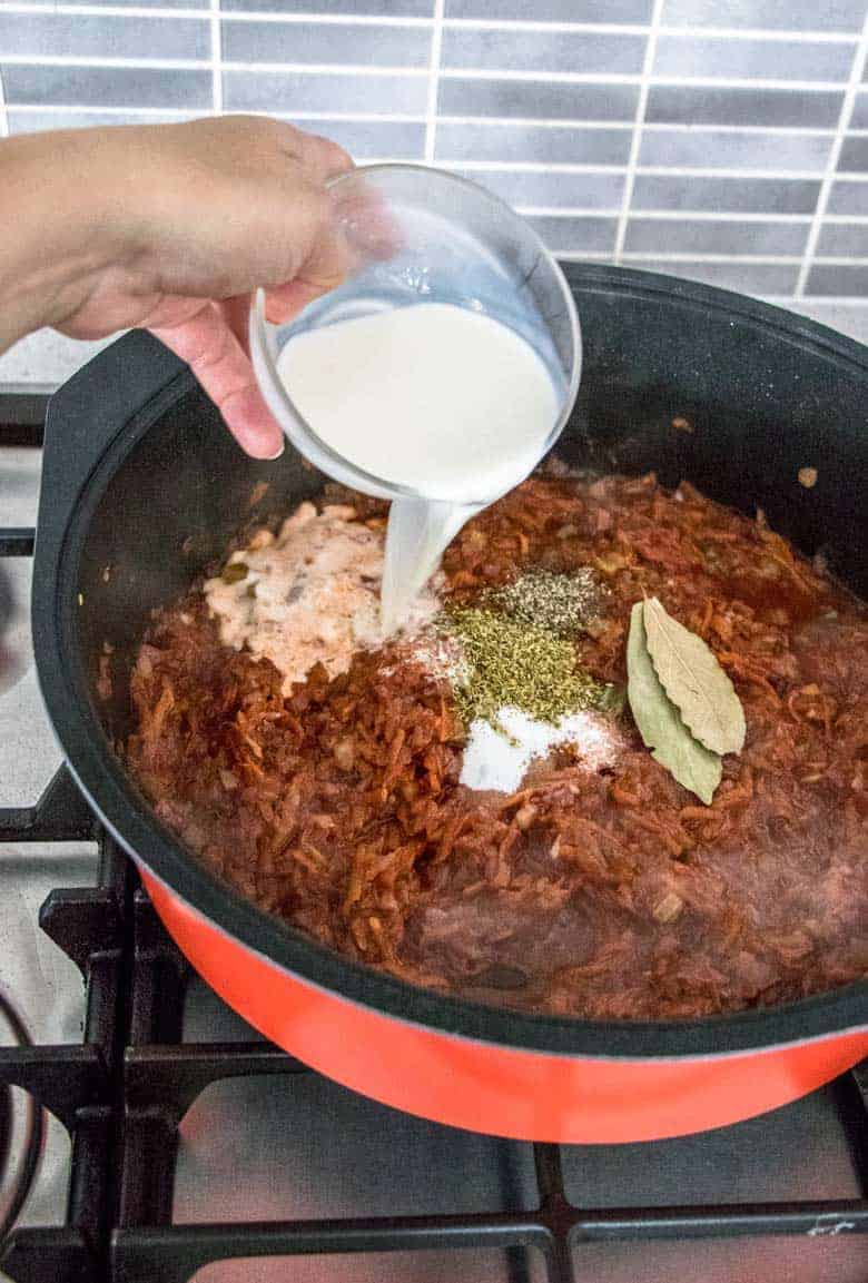 adding milk to ragu sauce in a pot