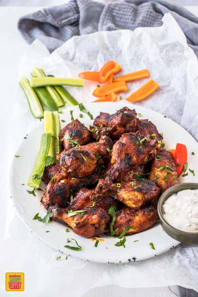 Crockpot chicken wings on a white plate with vegetables and sour cream