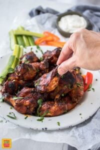 Picking up a single slow cooker chicken wing on a plate of wings