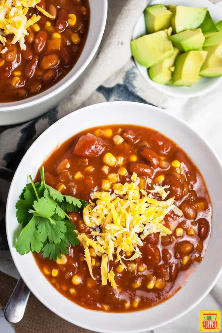 2 white bowls loaded with Slow Cooker Vegetarian Chili, shredded cheese, & garnished with cilantro and avocado