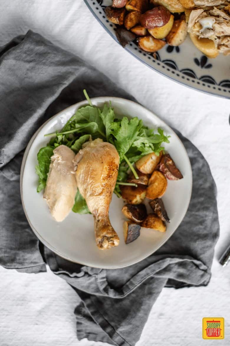 Slow Cooker Whole Chicken leg on a white with salad and roasted potatoes