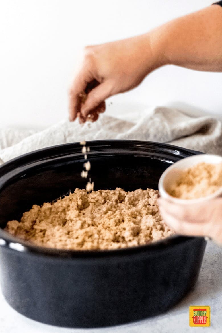 a woman sprinkling brown sugar on top of the slow cooker steel-cut oats
