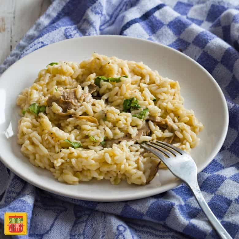 Instant pot risotto with mushrooms on a white plate with a fork sitting on a blue checker towel