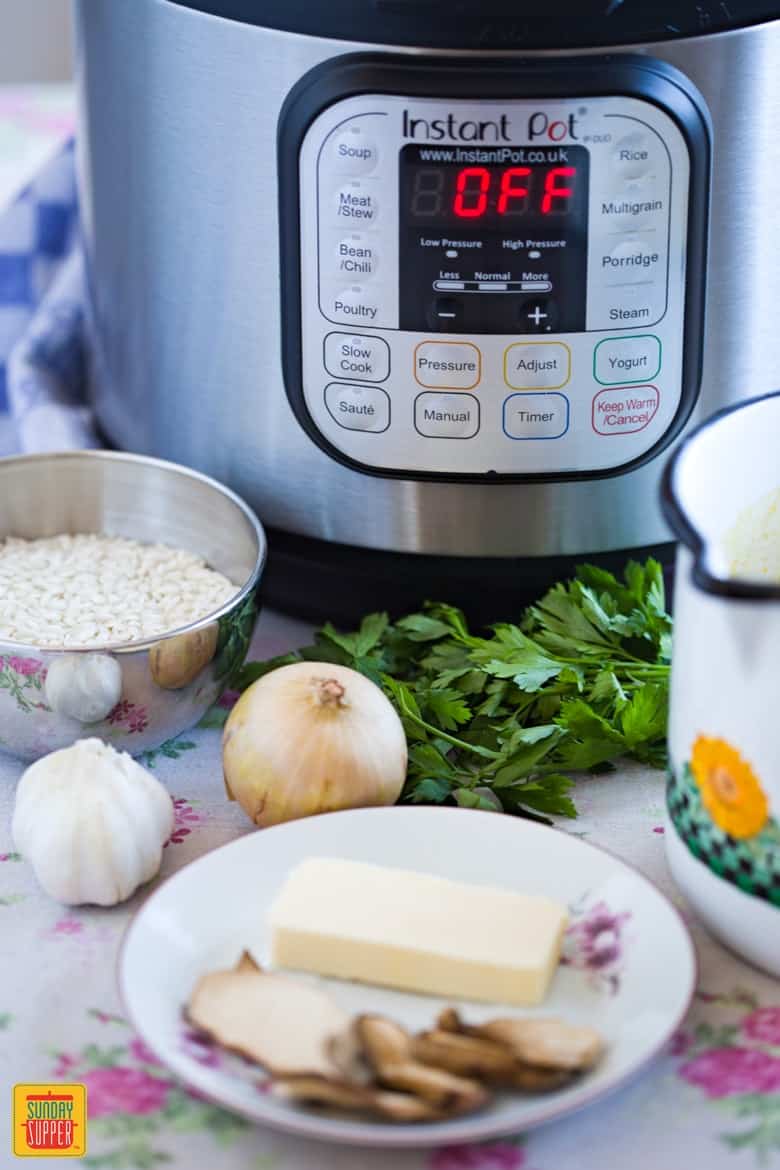 Ingredients for Instant Pot Risotto: parsley, onions, rice, butter, dried porcini mushrooms, broth and garlic sitting in front of the instant pot on the table