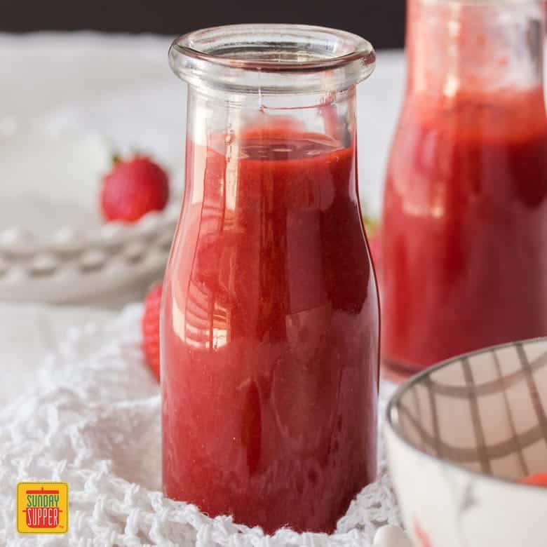 Strawberry sauce recipe in glass containers near strawberries and a doily