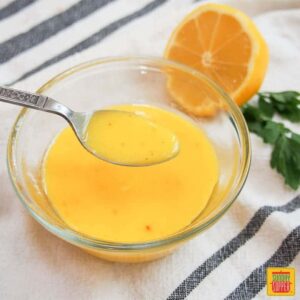 hollandaise sauce in a bowl with a spoon next to citrus and herbs