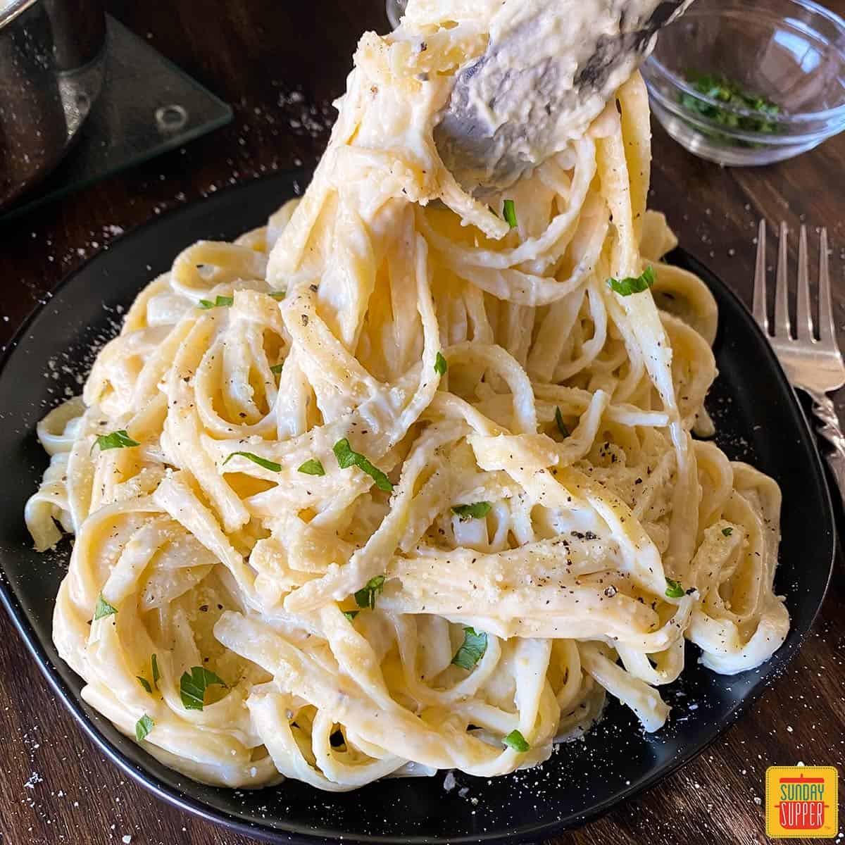 lifting creamy fettuccine alfredo off of a plate with tongs