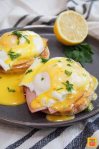 two eggs benedict on a gray plate with a sliced lemon