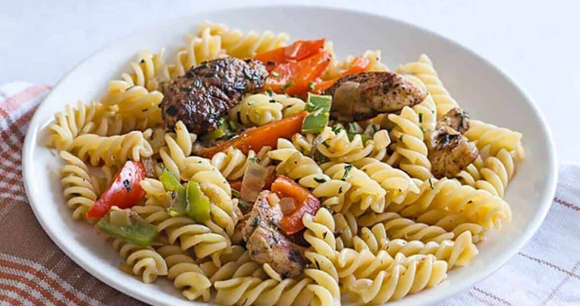 Rasta pasta recipe with jerk chicken, bell peppers, and fusilli pasta served on a white plate, ready to eat