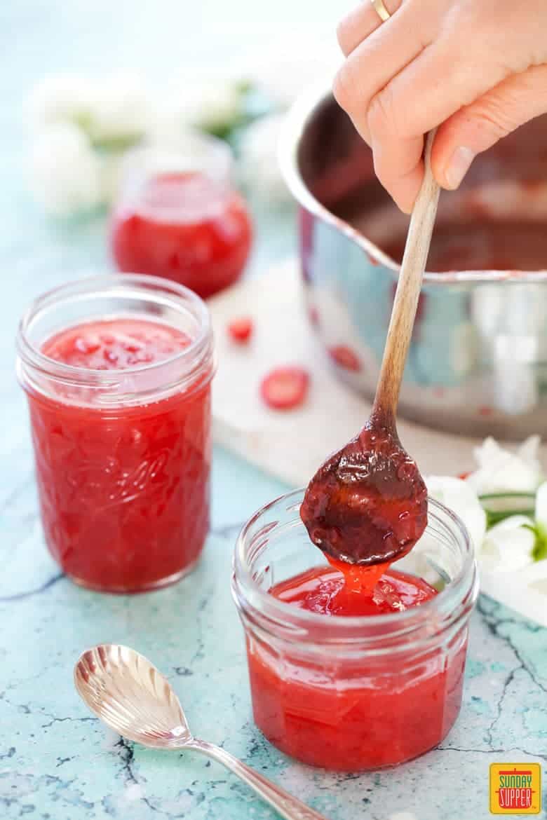 Strawberry rhubarb jam in jar with wooden spoon ladling out some jam