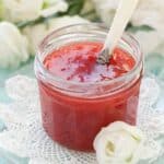 close up strawberry rhubarb jam in a clear jar with a metal spoon inside