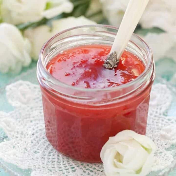 close up strawberry rhubarb jam in a clear jar with a metal spoon inside