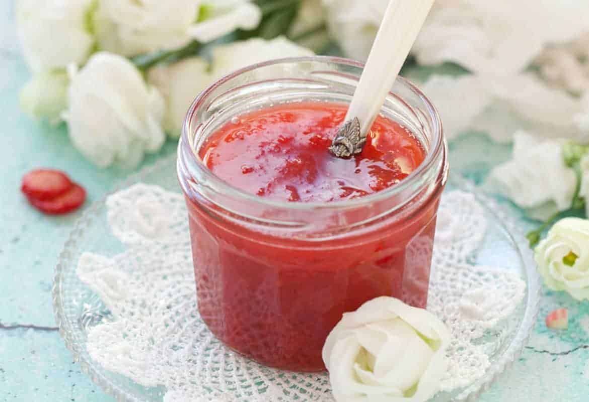 close up strawberry rhubarb jam in a clear jar with a metal spoon inside