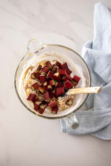 Adding rhubarb to cake batter in a large glass mixing bowl
