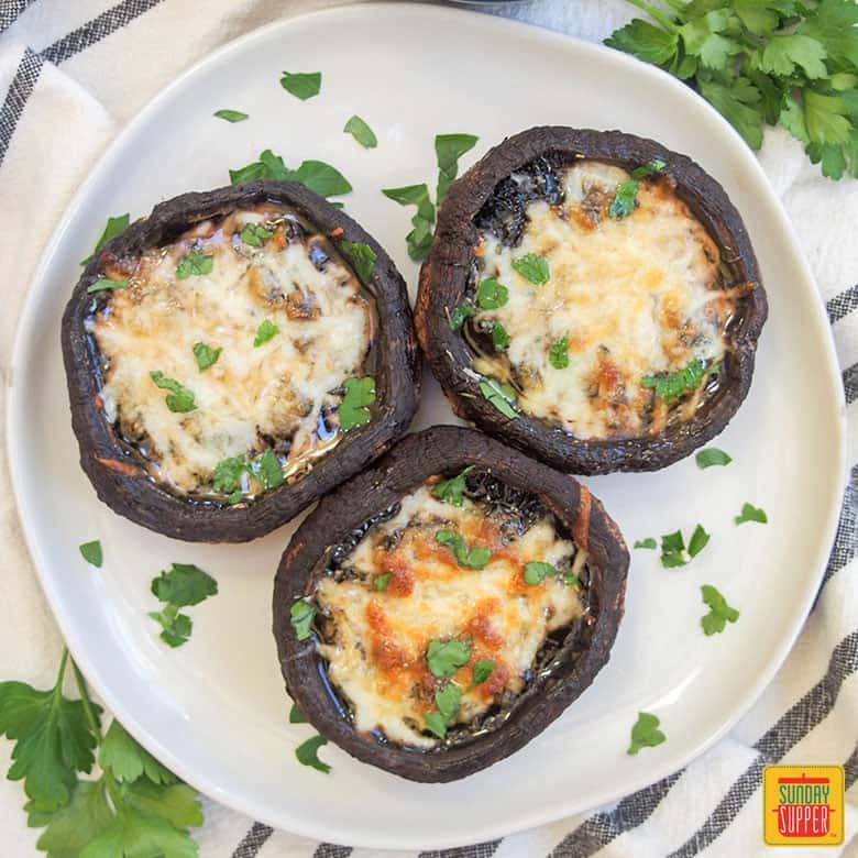 Three baked portobello mushrooms with cheese on a white plate