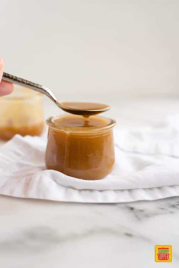Butterscotch sauce dripping off a spoon into a glass container