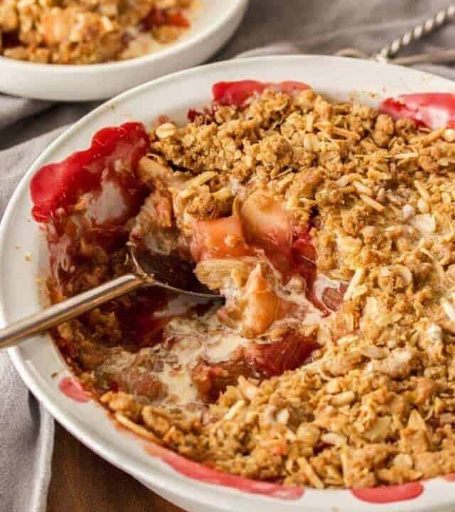 A rhubarb and apple crumble in a pie dish with a small serving in the background