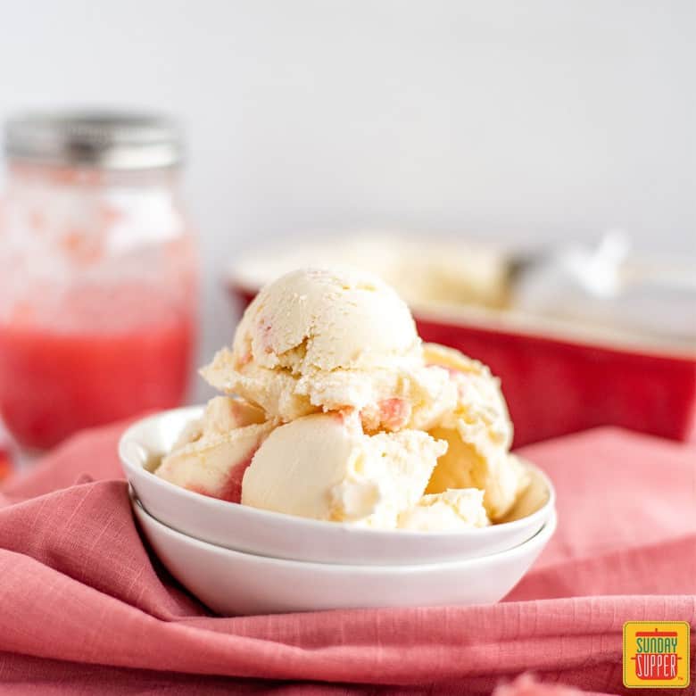 Rhubarb ice cream in a white dish with rhubarb sauce in a jar in the background
