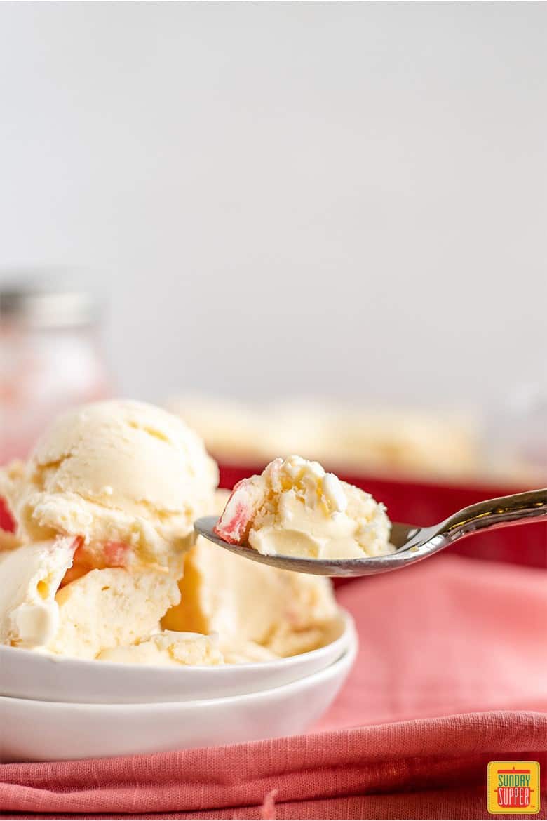 Rhubarb ice cream in a white dish with a spoon taking a bite