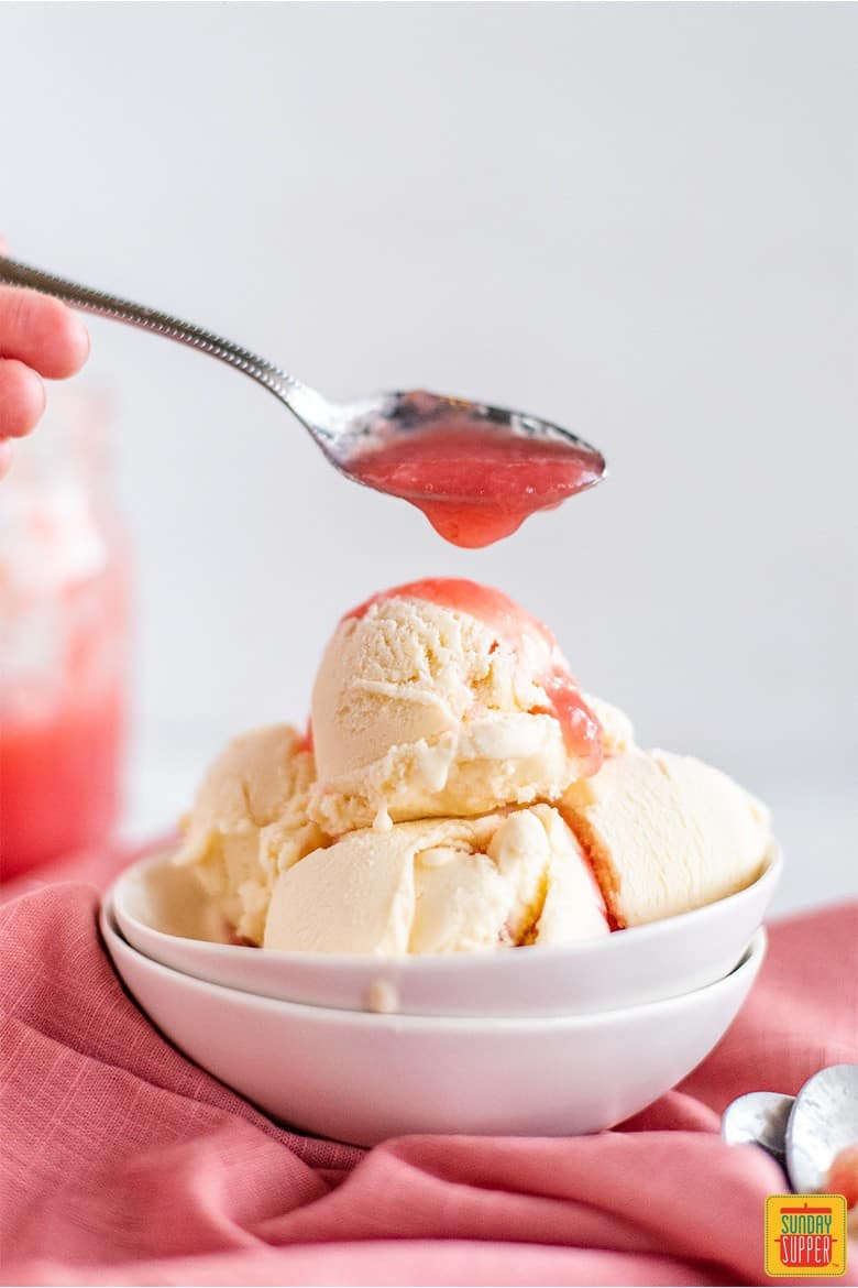 Topping rhubarb ice cream with homemade rhubarb sauce in a spoon