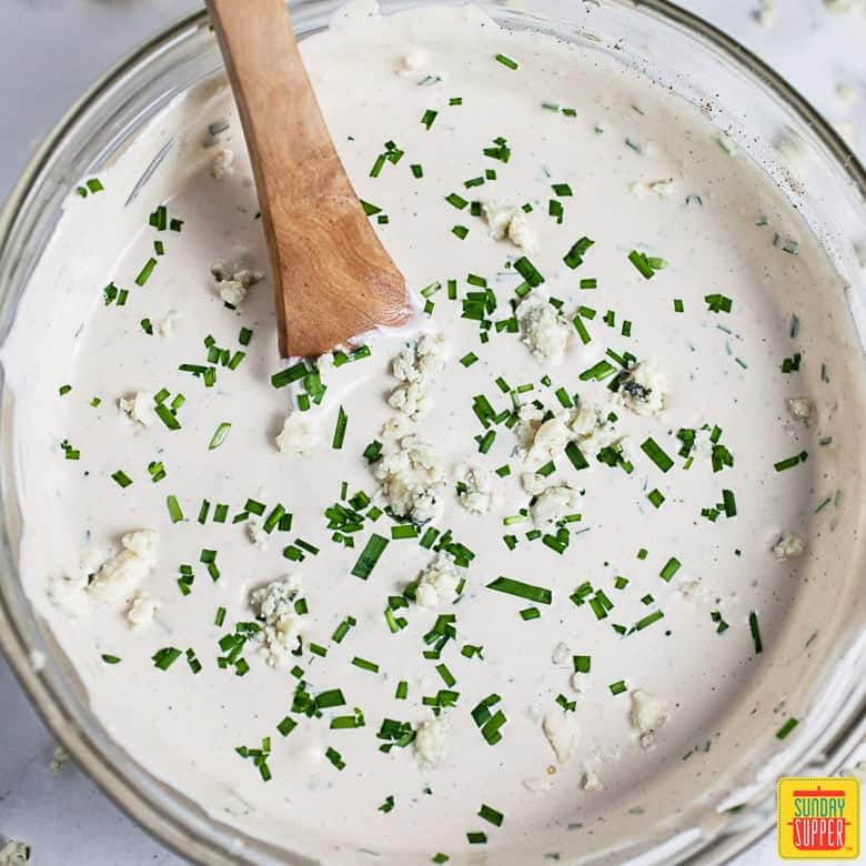 How to make blue cheese dressing: dressing in a glass bowl with a wooden spoon