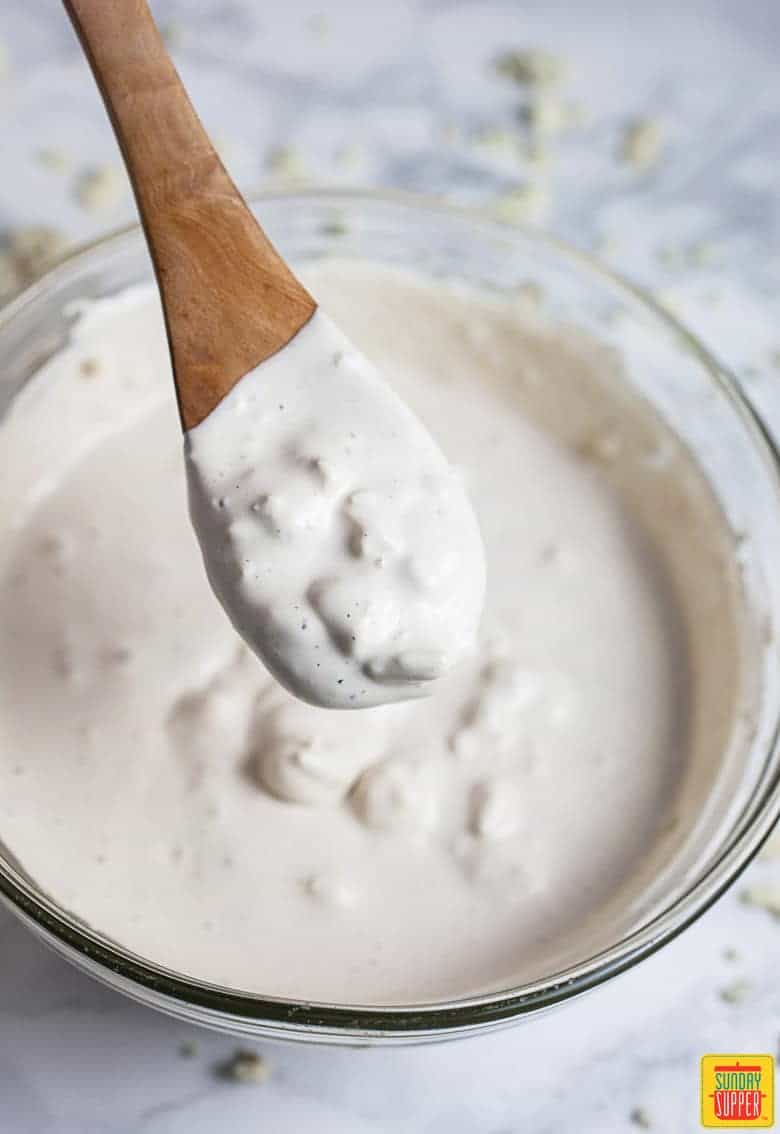 Blue cheese dressing in a bowl with a wooden spoon showing the consistency