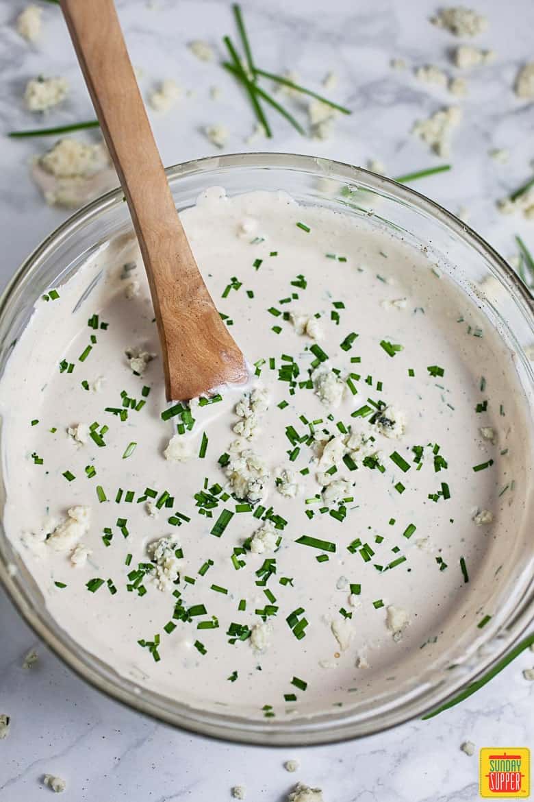 Blue cheese dressing in a bowl with a wooden spoon topped with chives