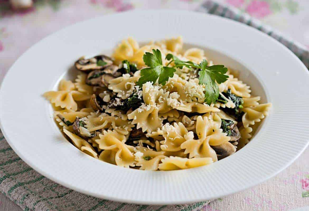 Mushroom spinach pasta on a white plate with parmesan on top