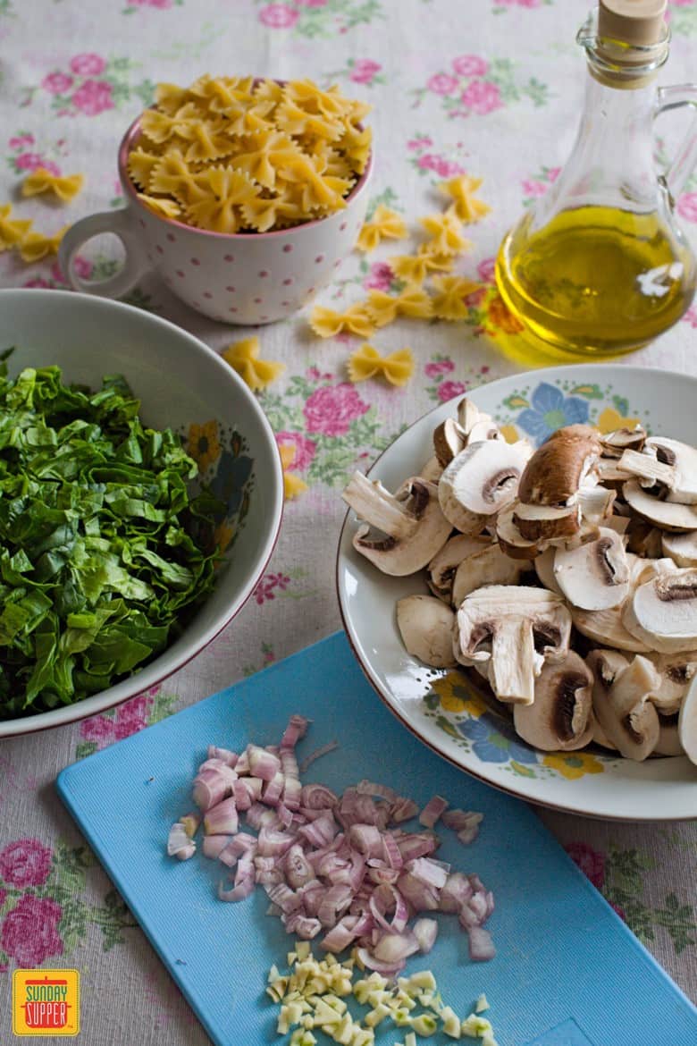 Ingredients for the mushroom spinach pasta in separate bowls on a floral tablecloth