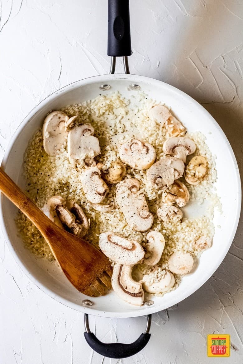 mixing mushrooms with rice for mushroom risotto recipe in white pan