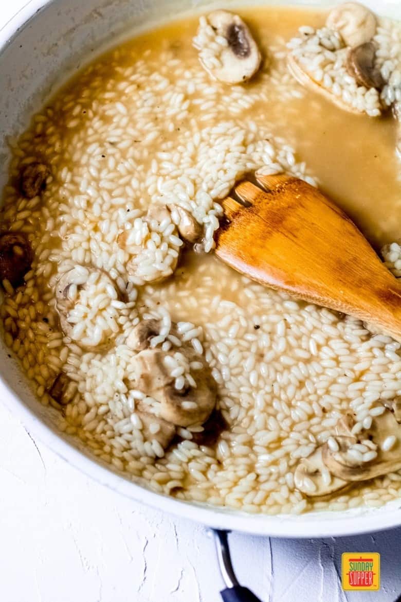 Stirring mushroom risotto recipe in a white pan with a wooden spoon