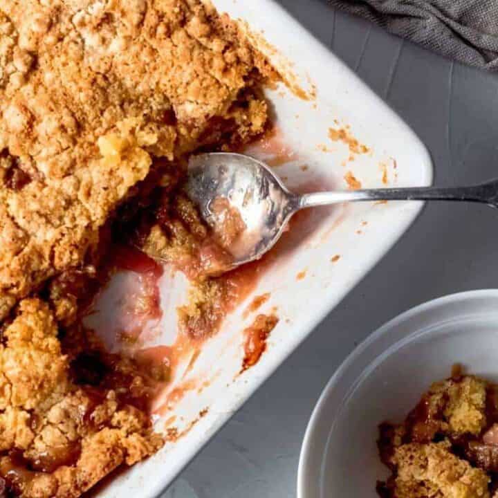 Rhubarb dump cake in a white baking dish with a serving spoon and a bowl of dump cake to the side