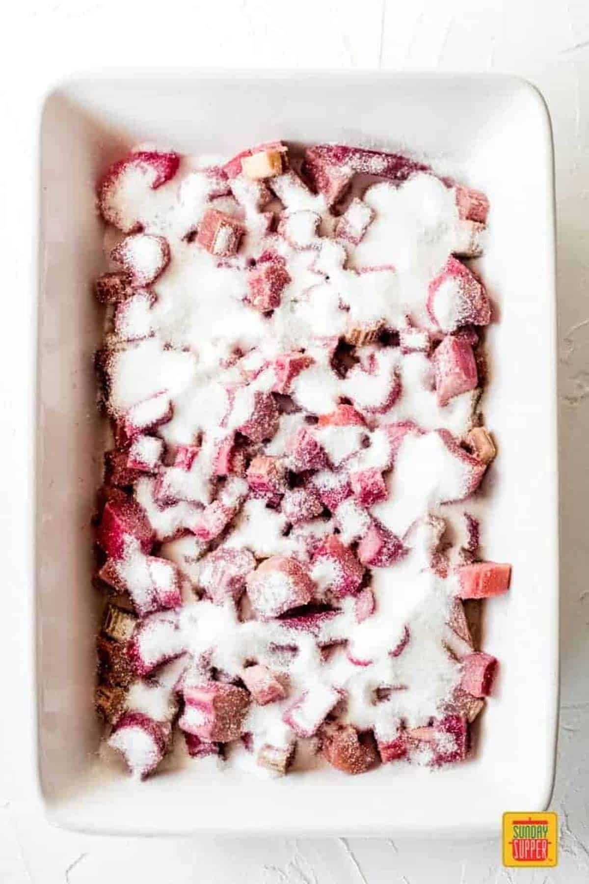 Sugar poured over the rhubarb slices in a white baking dish