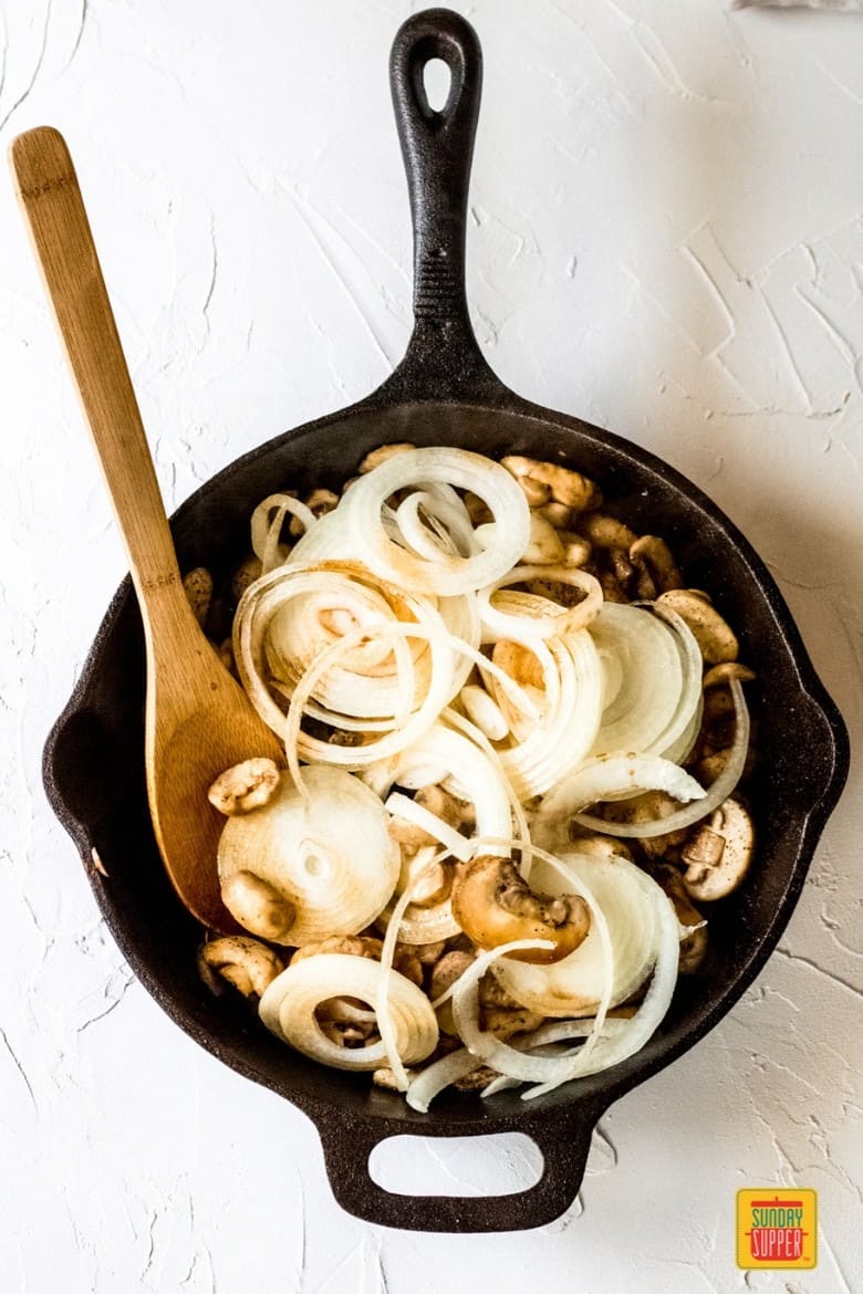 mushrooms and onions cooking in a black cast iron
skillet with a wooden spoon for sauteed mushrooms and onions