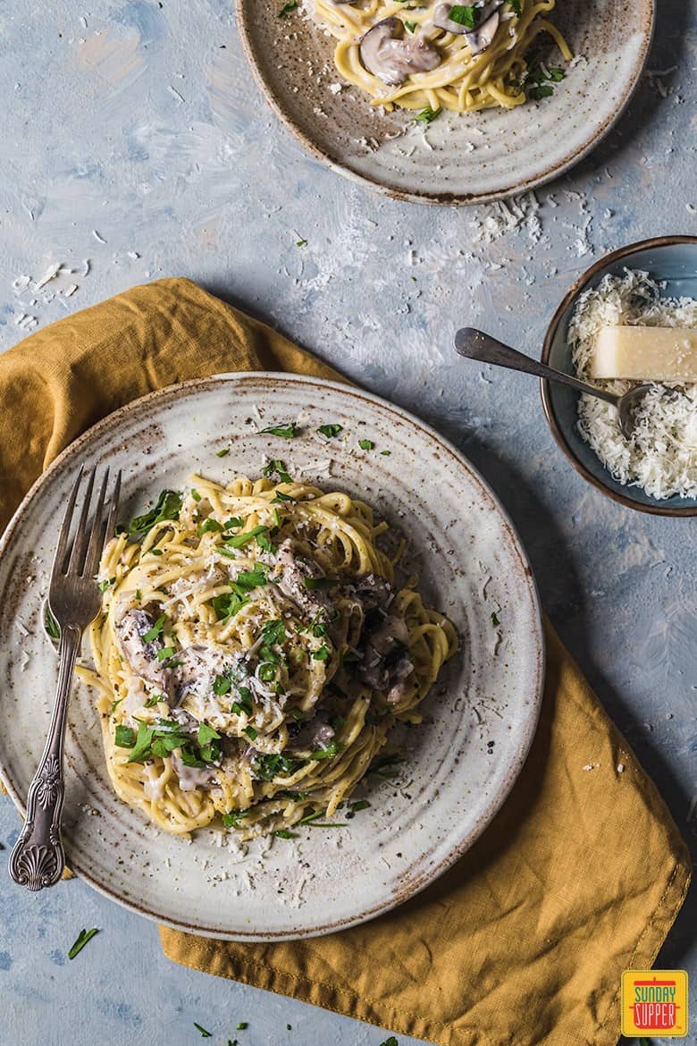 spaghetti in mushroom sauce served on ceramic plates with a fork and grated parmesan