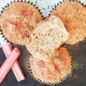 Four rhubarb muffins stacked next to two slices of fresh rhubarb