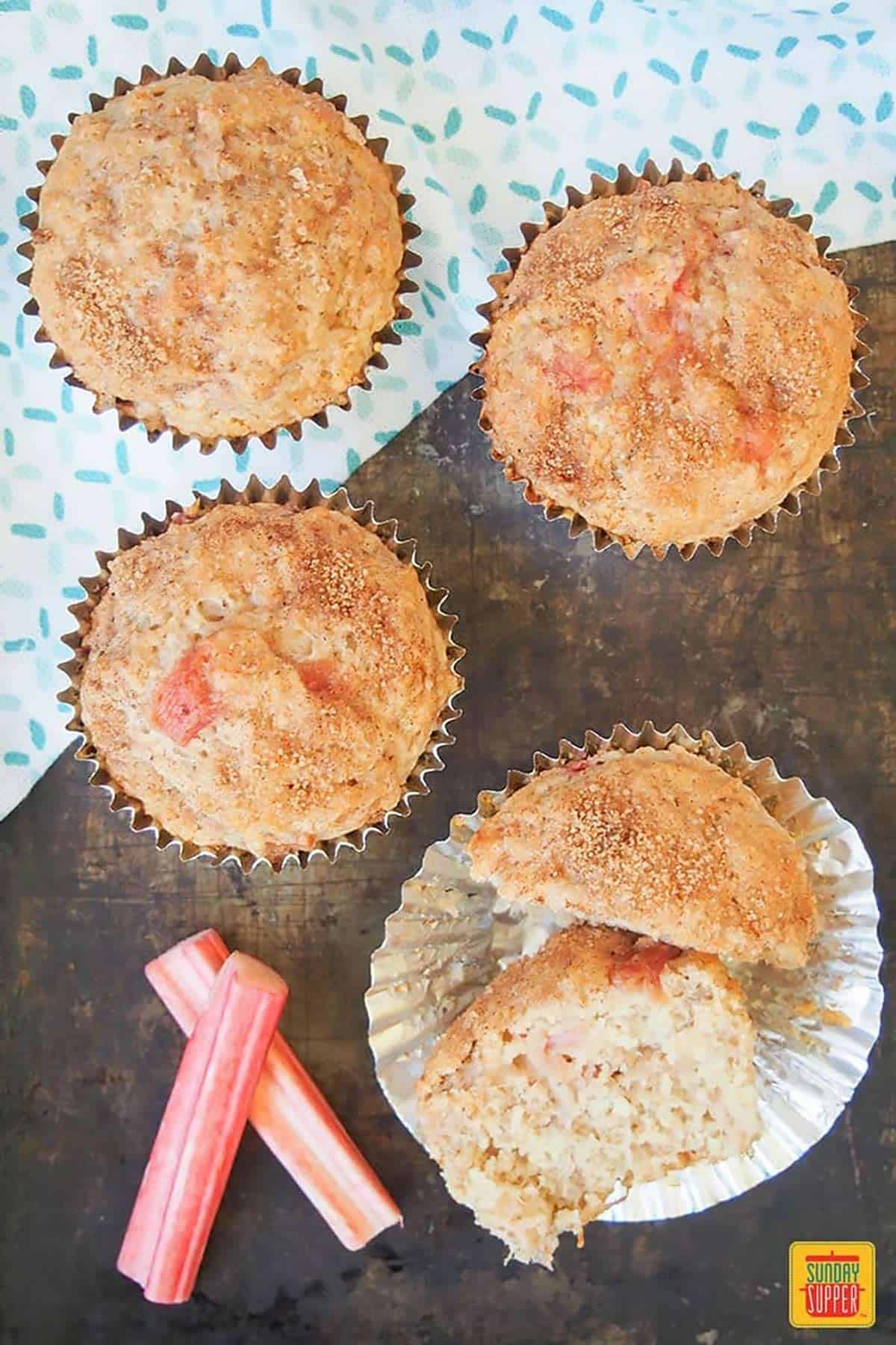Four rhubarb muffins: one is split in half in a muffin mold to show how soft it is
