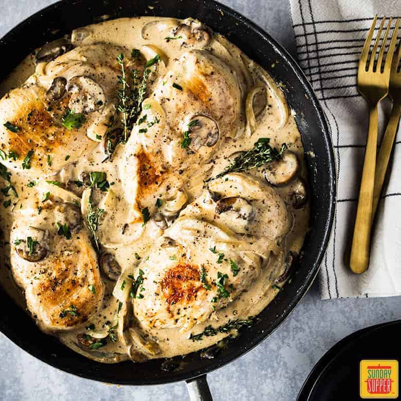 chicken breast and mushroom recipe in pan with fresh parsley and thyme for garnish