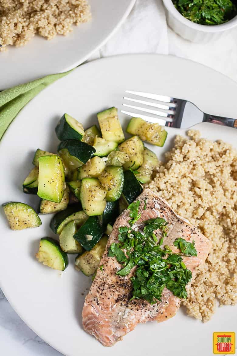 A fillet of cooked salmon with fresh gremolata and roasted vegetables on a white plate with a fork