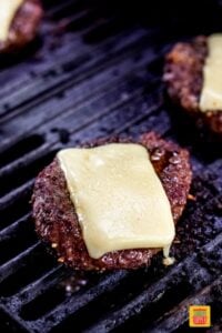 bison burgers on the grill topped with gruyere cheese