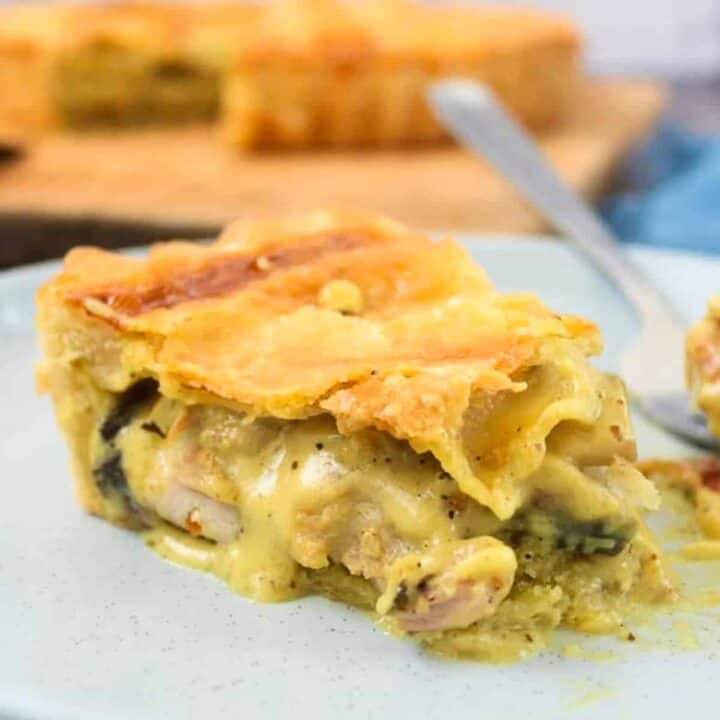 Slice of chicken pie recipe on a light gray plate with a fork and the whole pie visible in the background