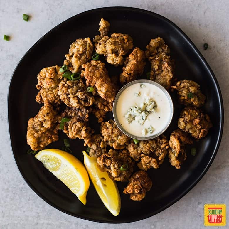 Fried Oysters Recipe on a black plate with blue cheese and lemon wedges