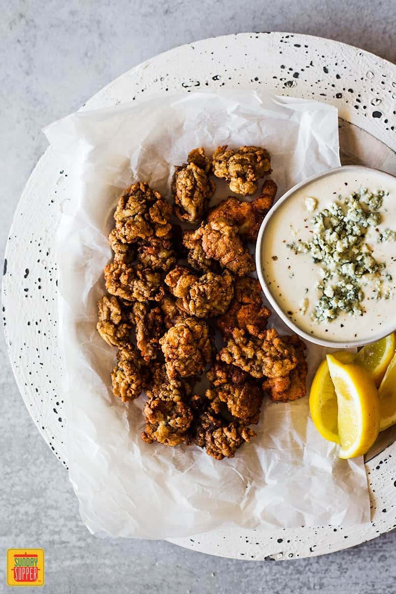 Pan fried oysters in a white dish with blue cheese dressing and lemon wedges
