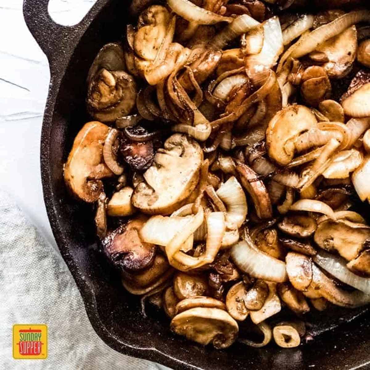 Sauteed Mushrooms and Onions in a black skillet, caramelized and ready to serve