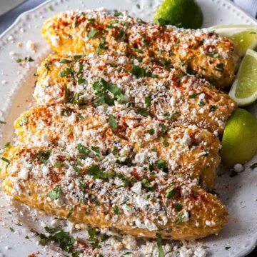 Four grilled corn, topped with cheese on a white plate.