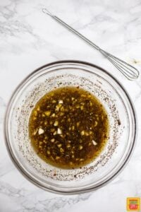 Steak marinade for grilled chuck steak in a glass bowl with a tiny whisk nearby