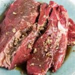 Uncooked chuck steak in marinade on a light blue platter