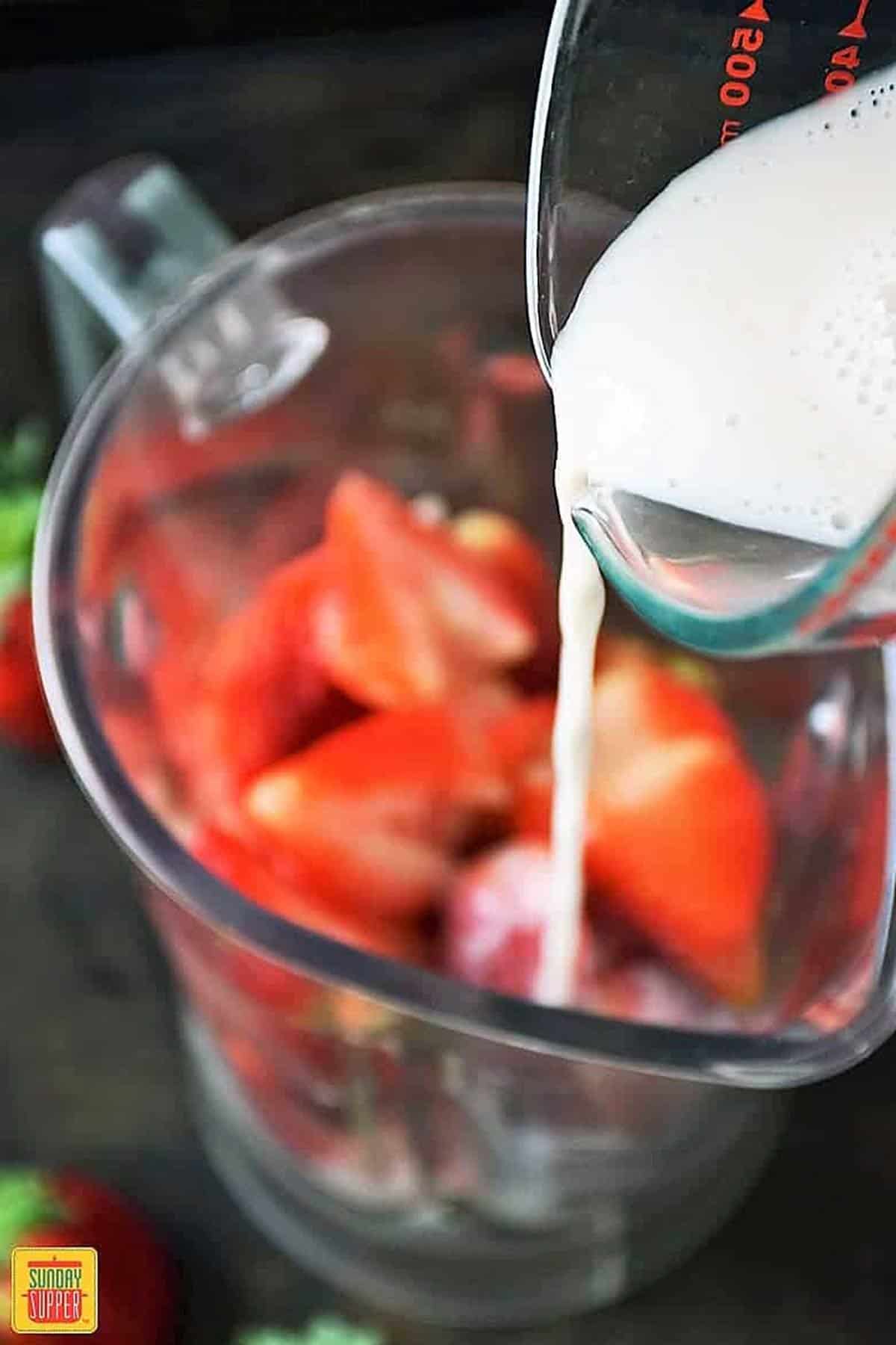 Pouring almond milk into blender with the fresh strawberries